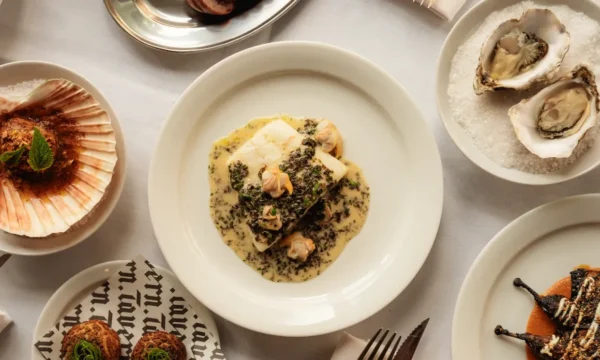 An array of dishes, in the centre is a piece of fish in sauce. Other dishes include oysters, scallops and croquettes.