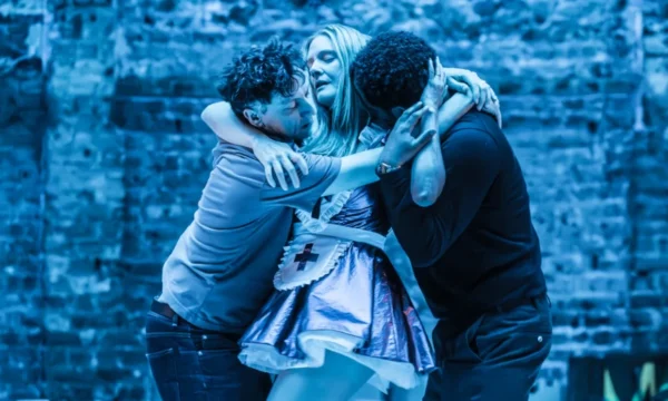 Main character Nora is embraced by both her husband and best friend in a dramatic shot.