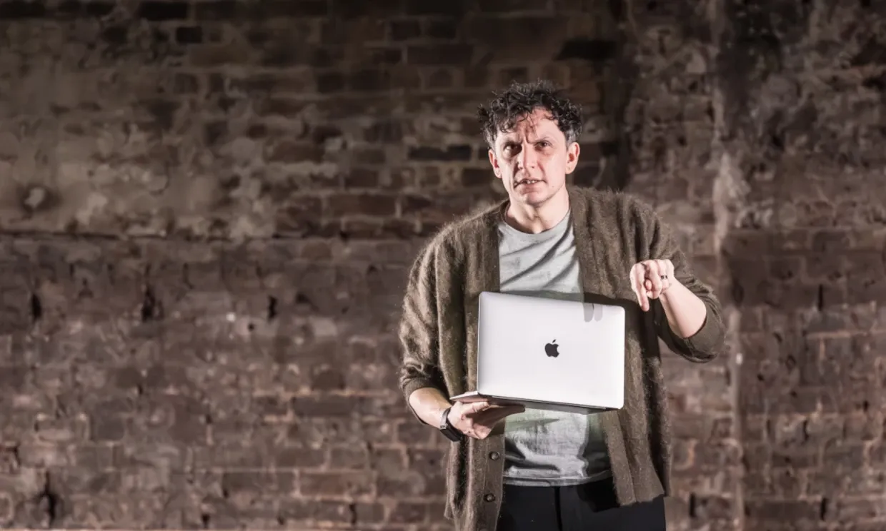 Nora's husband Torvald is gesticulating while holding a macbook.