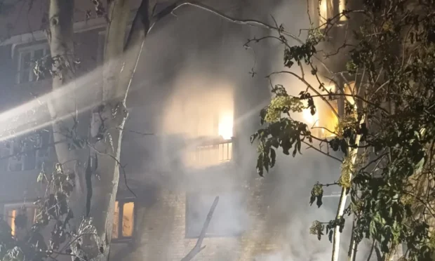 Smoke is visible outside as a fire lights up flat windows