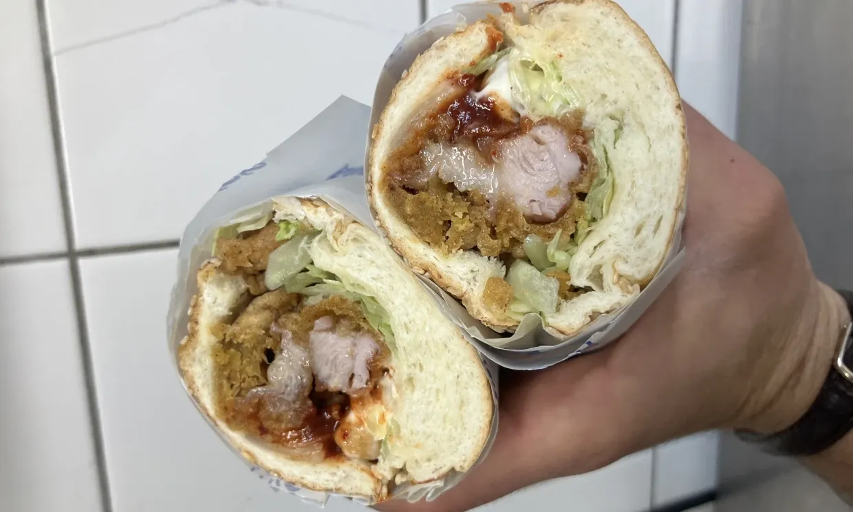 Close up of a cut-open sandwich, filled with a meat, salad, sauce.