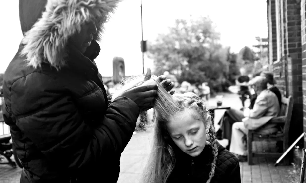 A woman braids a young child's hair in the street.