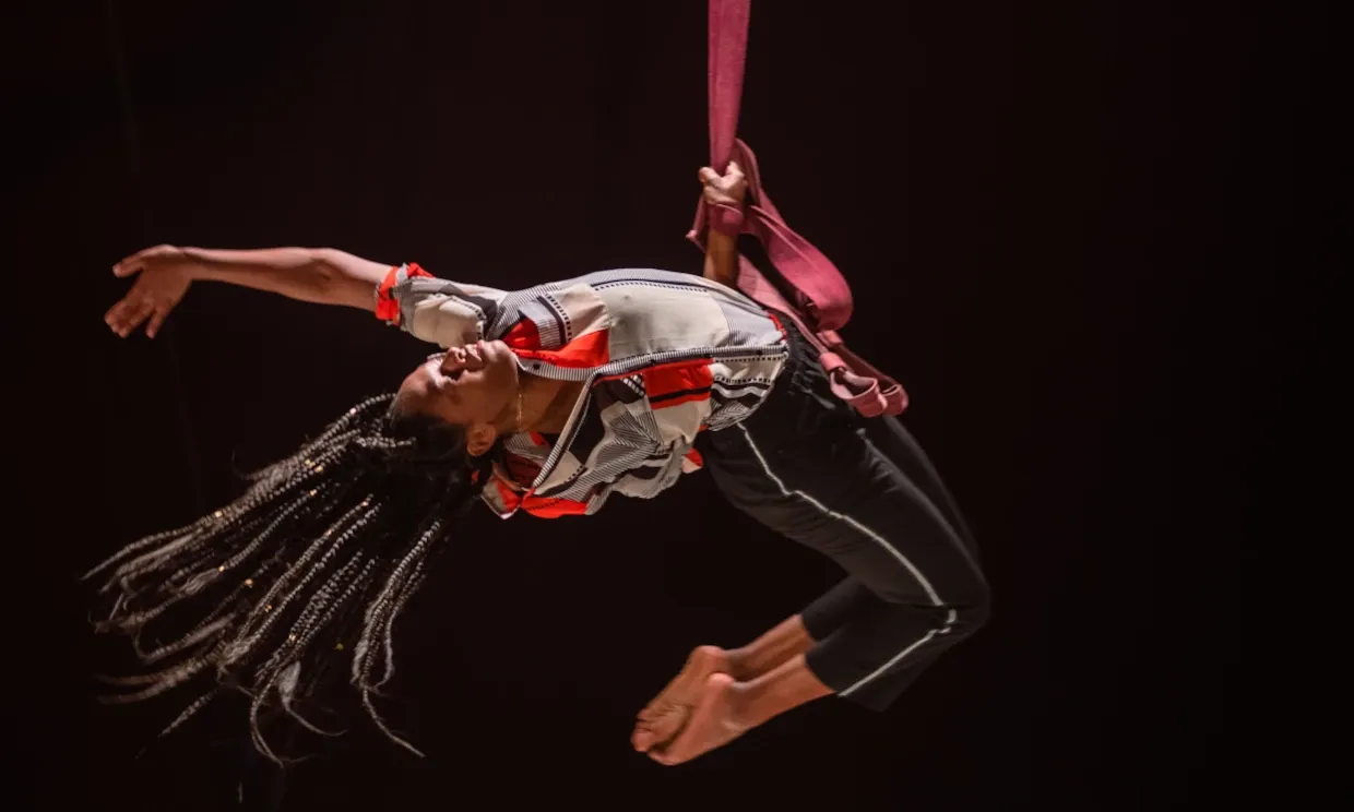 A woman suspends in the air from a ribbon.