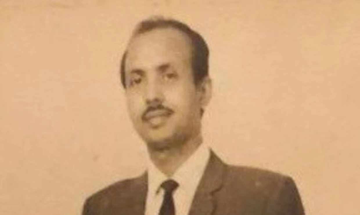 An old black and white portrait of Ishaque Ali, he is wearing a suit and smiling