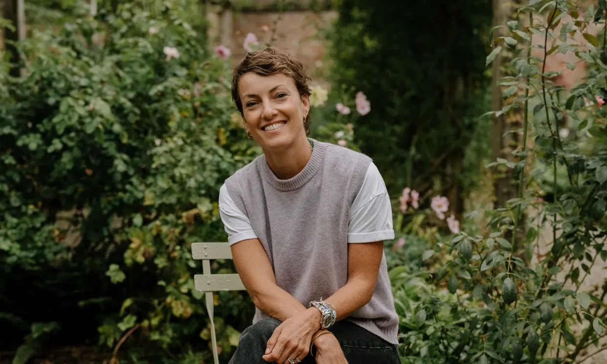 Photo of Lottie Delamain, a young woman sitting in a garden smiling