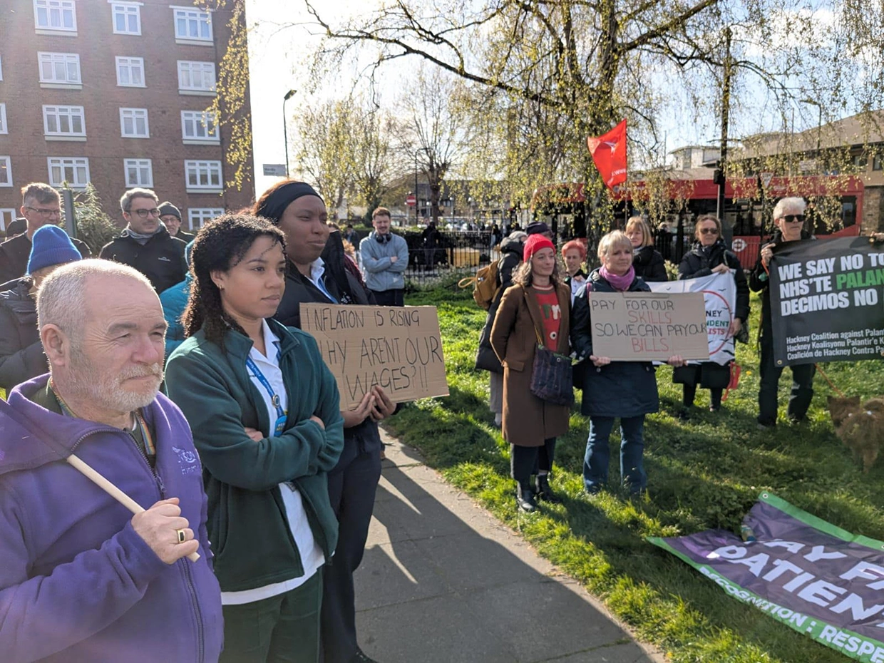 Protestors stand with placards and signs outside Homerton Hospital. "Pay for our skills, so we can pay our bills", one of the signs reads.