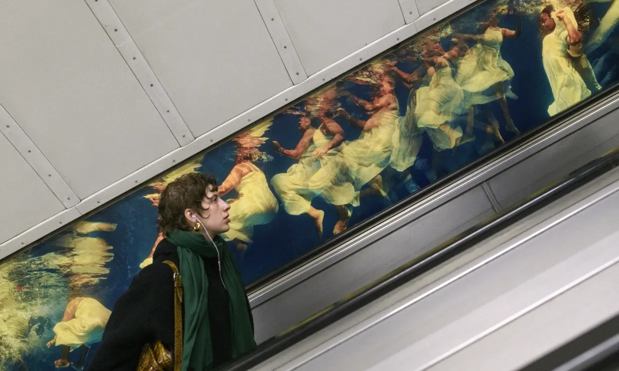 Phoebe's artwork features behind someone going up the escalator on the tube
