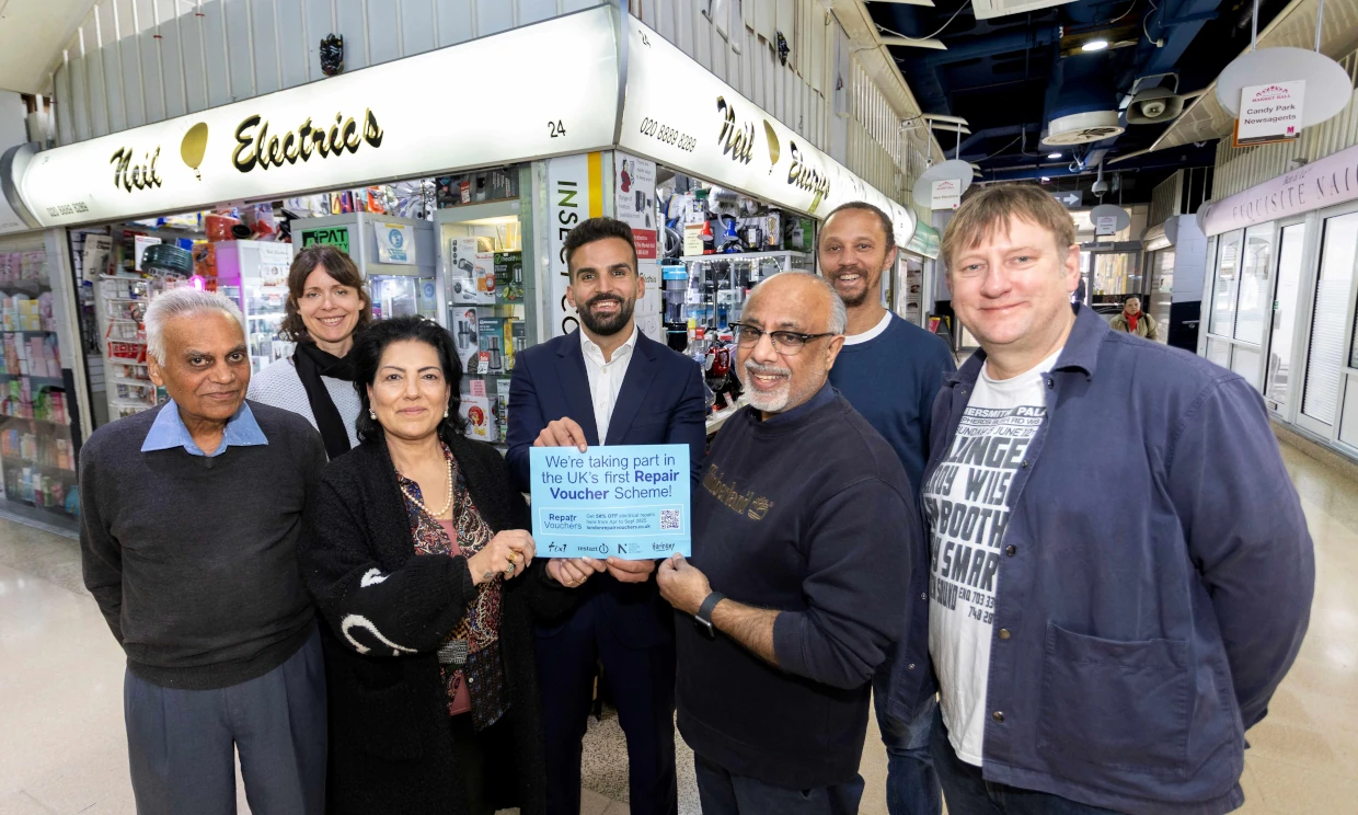 Staff of Neil Electrics hold a Repair Voucher outside the store.