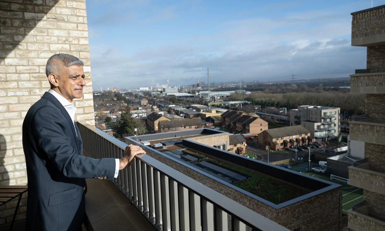 Sadiq Khan standing on a balcony, looking out over housing complexes.