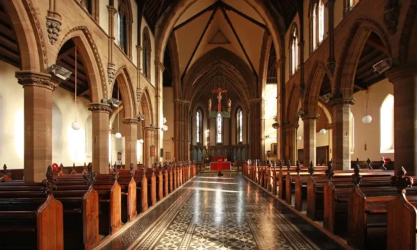 The interior of a church. Rows of brown wooden pews, with an ornate floor and beige coloured walls and ceiling