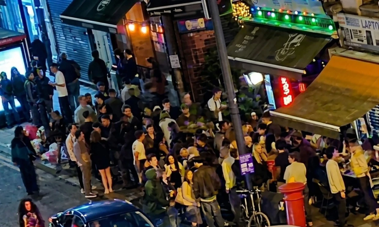 A crowd of people queue outside a club.