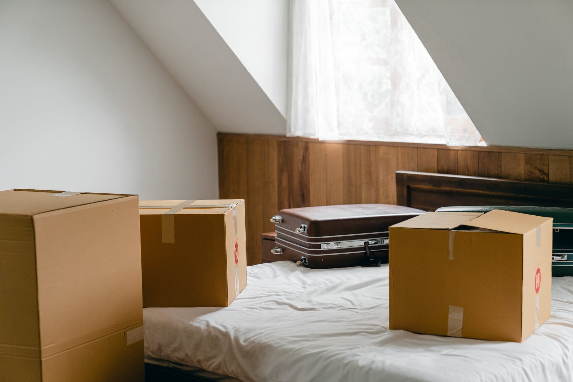 carton boxes and suitcases placed on bed in empty light room
