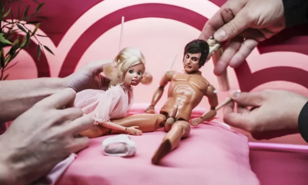A close up shot of two small doll-like puppets, being worked by human hands. One is a female puppet leant over a naked male puppet